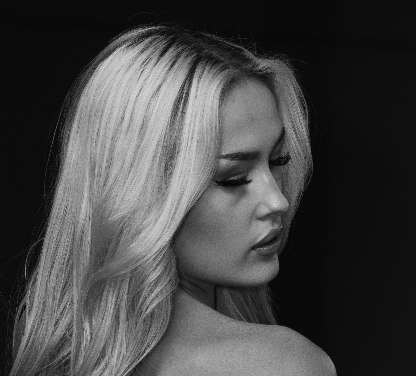 Black and white portrait, eyes lowered, rim light catching her hair against a dark background